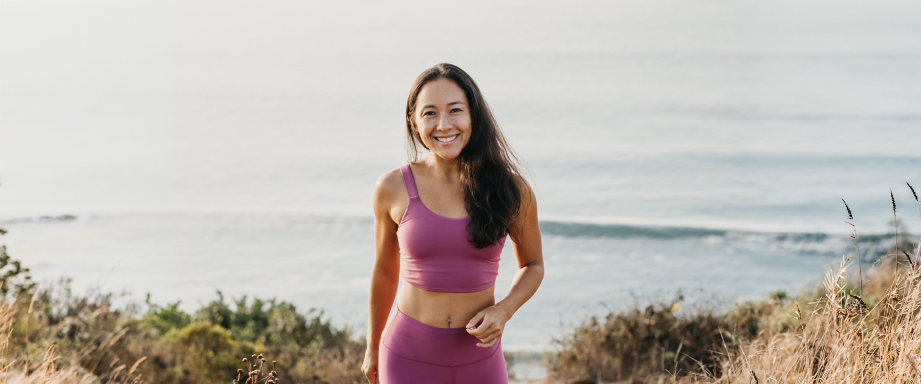 Briohny Smyth standing on a coastal path in yoga wear, from the Aligned Yoga website